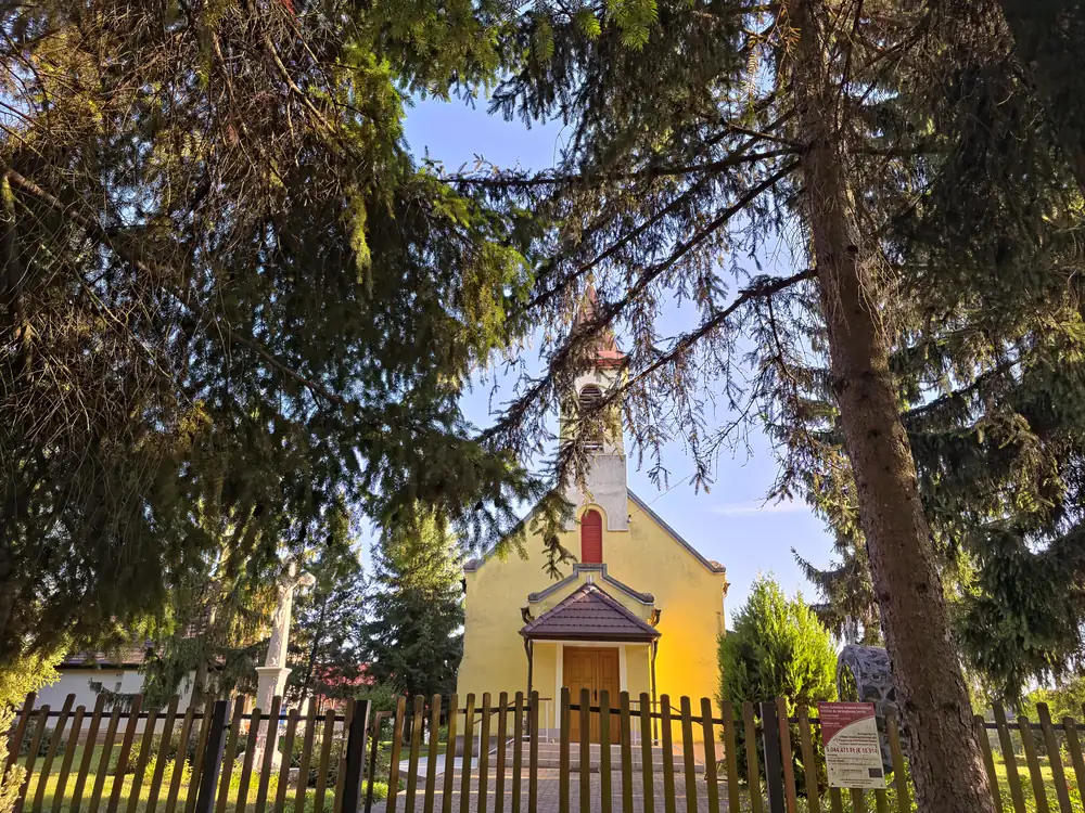 A Szent Lukács templom tornya fák között Szügyön